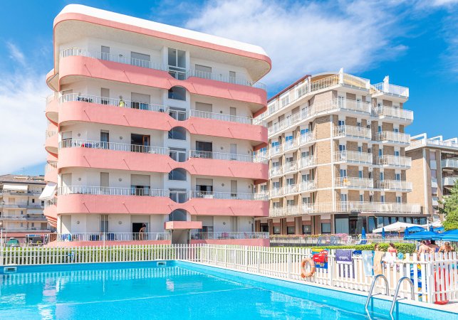 Edificio rosa e bianco con piscina in primo piano.