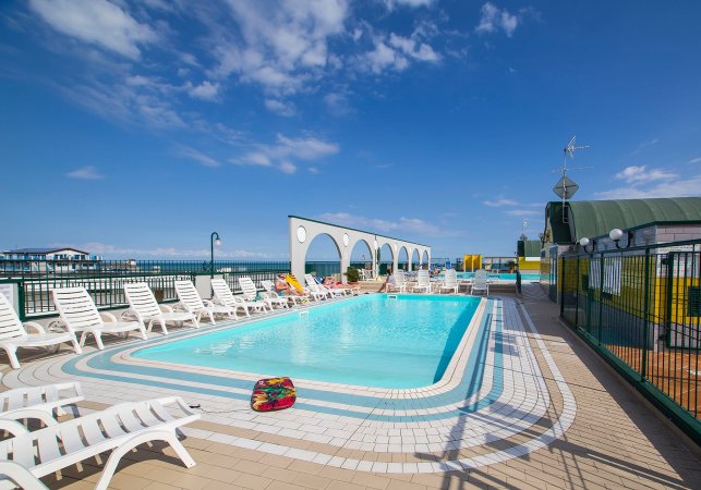 Piscina con lettini bianchi e cielo blu.