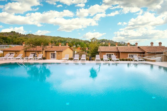 Piscina all'aperto con sdraio e villette in lontananza.