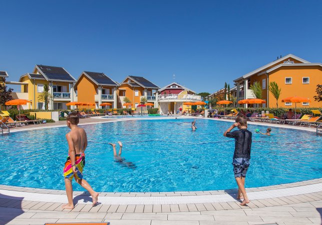 Ampia piscina circondata da edifici e ombrelloni.