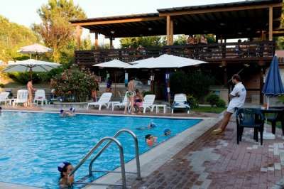 Piscina con ombrelloni bianchi e una terrazza coperta in legno. Persone vicino e dentro l'acqua.