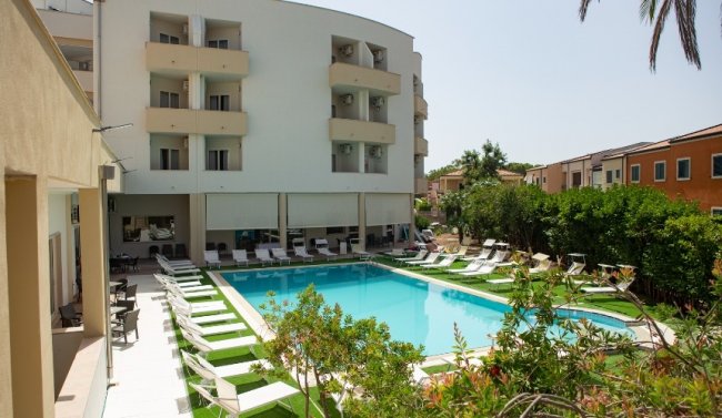 Piscina all'aperto con lettini, di fronte a un edificio a più piani.