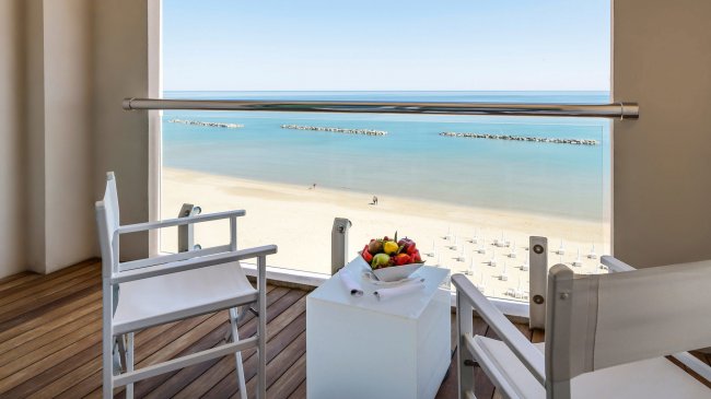 Vista mare con sedie, tavolino e frutta su un balcone.