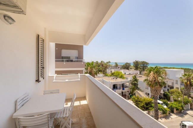 Balcone con tavolo e sedie, vista su edifici e mare.