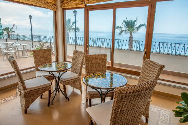 Sala da pranzo con vista mare e tavoli di vimini.