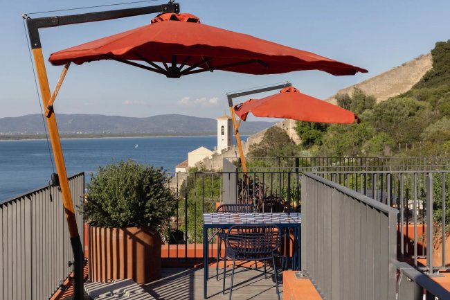 Terrazza con tavolo, sedie e ombrelloni rossi sul mare.