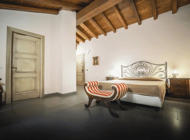 Camera con letto matrimoniale, panca a strisce e soffitto in legno.