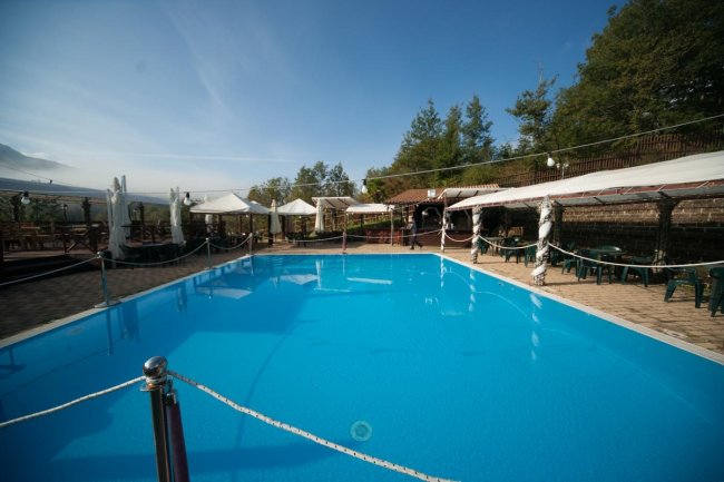 Piscina esterna con tende e sedie verdi.