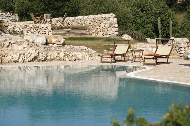 Piscina con sedie a sdraio e muretti in pietra.