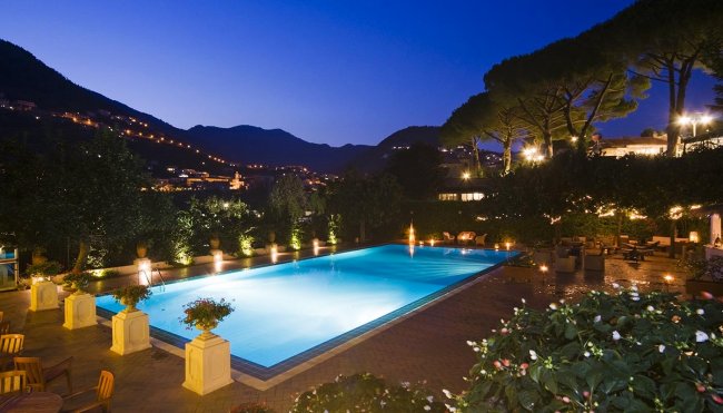 Piscina illuminata di notte con montagna sullo sfondo.