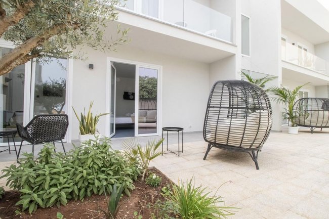 Patio con sedie di vimini, piante e ingresso a una stanza.