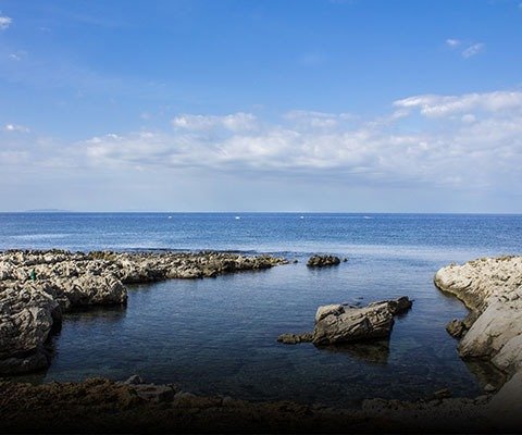 Costa rocciosa affacciata su un mare calmo sotto un cielo blu.