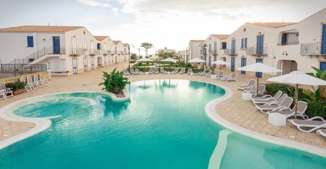 Piscina circondata da lettini in un resort con villette.
