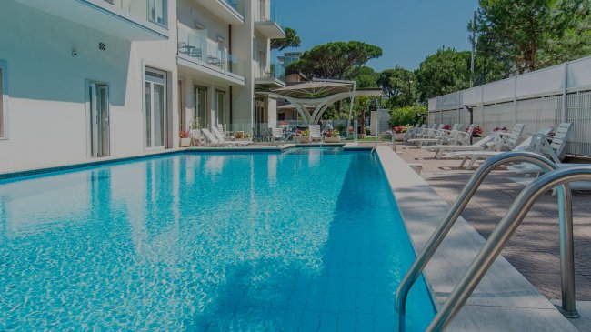 Piscina all'aperto con sdraio, circondata da alberi.