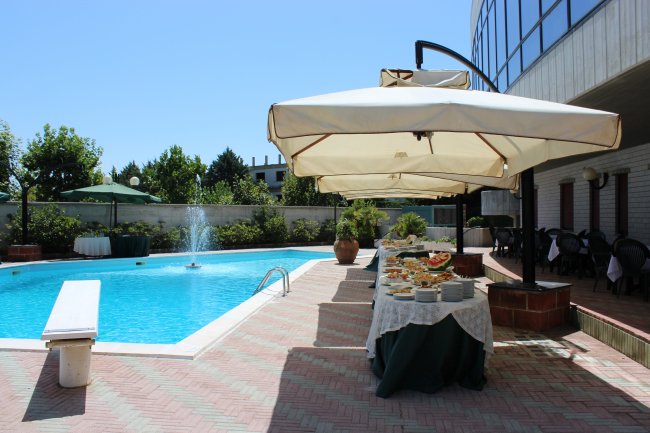 Piscina esterna con tavolo buffet e ombrelloni bianchi.