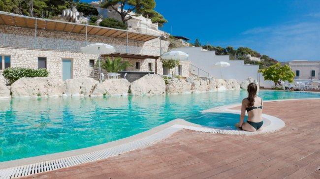 Piscina con donna seduta, sfondo pietra.