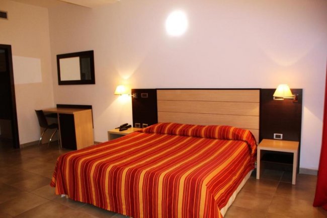 Letto matrimoniale con copriletto a righe e scrivania a sinistra.