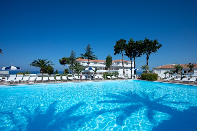 Una grande piscina con sdraio e alberi sullo sfondo.