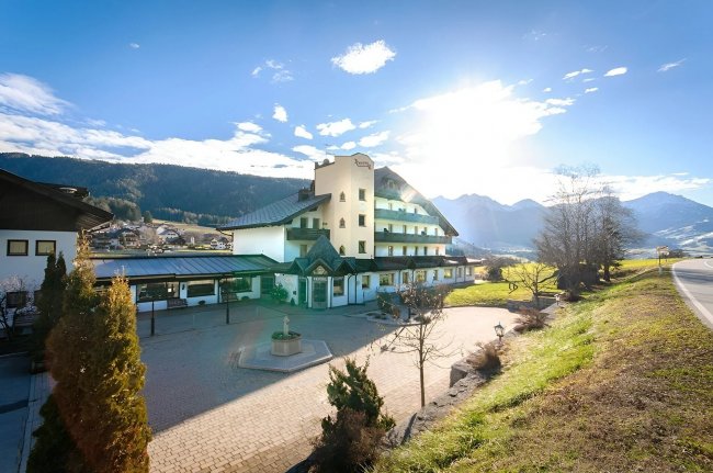 Hotel pittoresco con molte finestre, sotto un cielo soleggiato e montagne sullo sfondo.