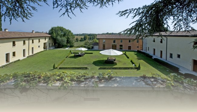 Ampia area verde con tavoli e ombrelloni tra edifici.