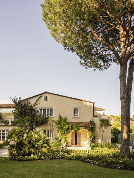 Villa beige con giardino e alberi, vista esterna.