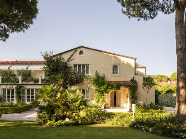 Edificio beige con giardino e vegetazione rigogliosa.