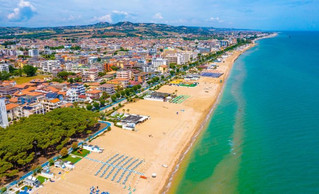 Lunga spiaggia sabbiosa con mare azzurro e case nella città attigua.