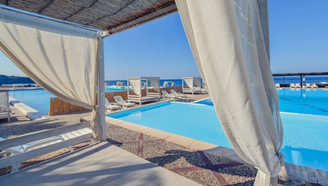 Piscina vista mare con tende bianche.