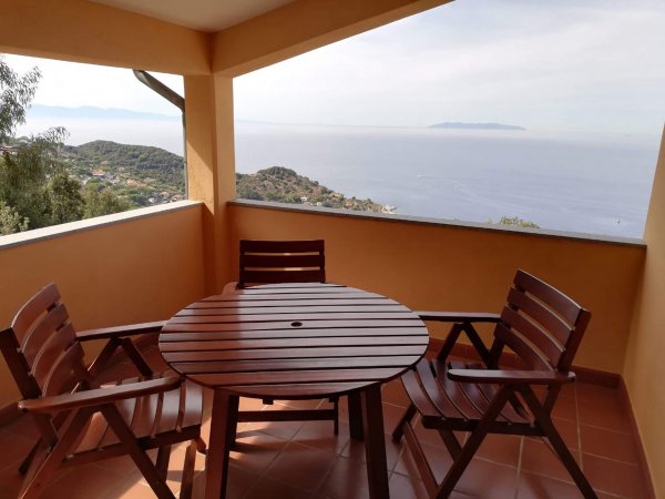 Tavolo rotondo e sedie in legno su terrazza con vista mare.