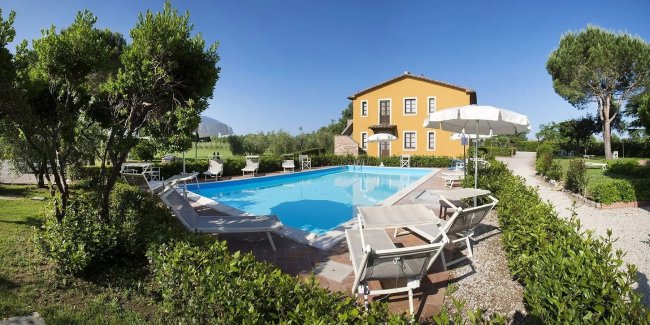Piscina luminosa con lettini e ombrelloni, vista su prato.