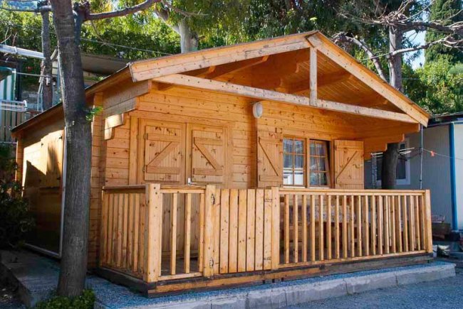 Esterno chalet in legno con veranda, circondato da alberi.