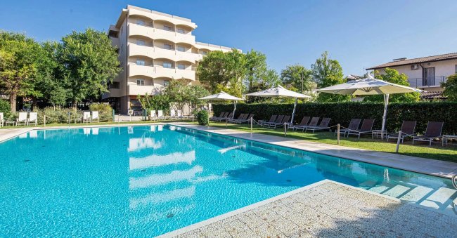 Piscina circondata da sdraio e ombrelloni, edificio in lontananza.