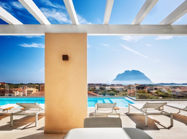 Vista di una piscina con sedie a sdraio e montagna sullo sfondo.