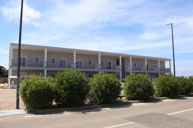 Edificio a due piani con balconi e vegetazione.