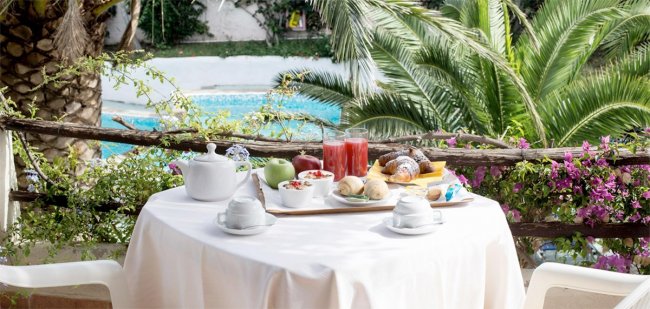 Tavolo con colazione e vista su piscina e palme.
