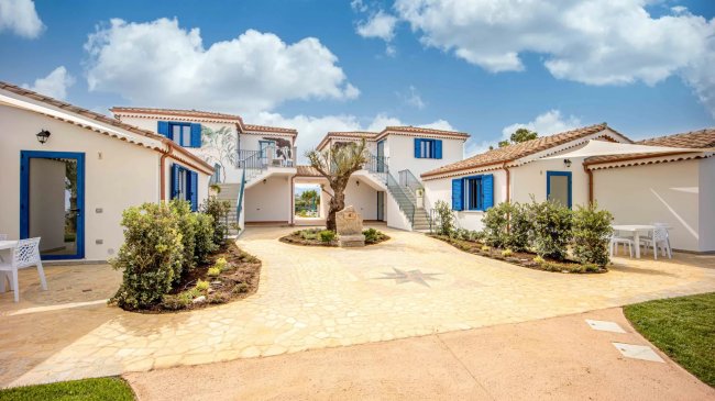 Cortile con case bianche, persiane blu, scala e pianta centrale.