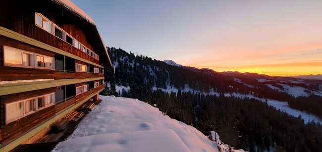 Edificio di legno su montagna innevata al tramonto.