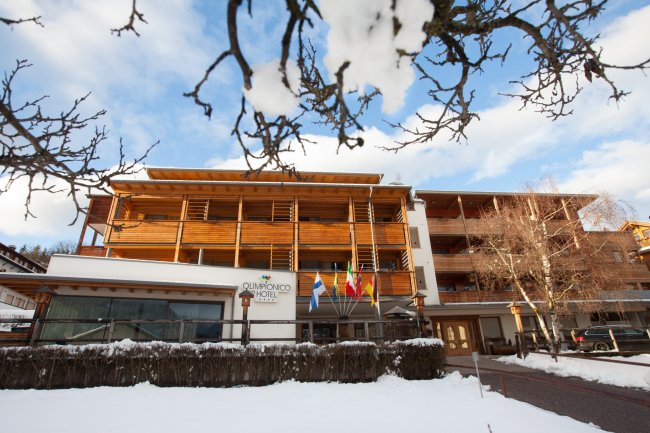 Facciata di un hotel in legno con bandiere all'ingresso, circondato dalla neve.