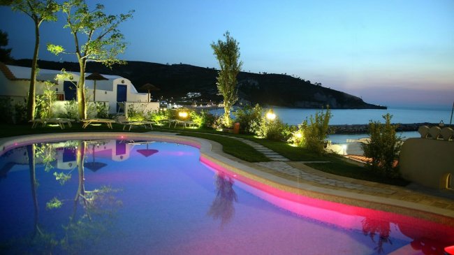 Piscina illuminata al tramonto con vista sul mare.