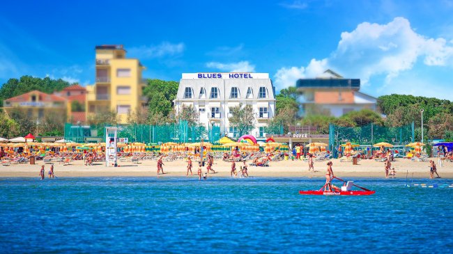 Spiaggia affollata con hotel bianco sullo sfondo.