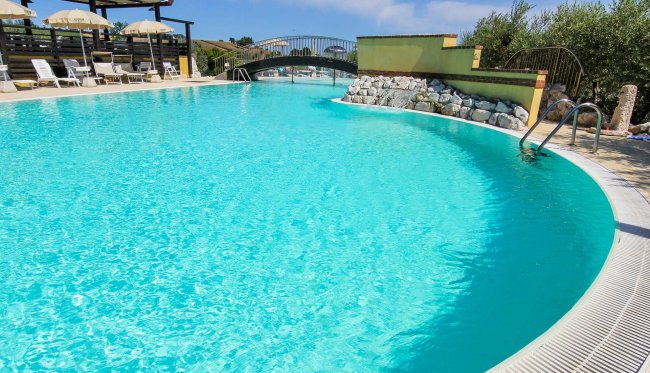 Piscina turchese con sedie a sdraio e ombrelloni.