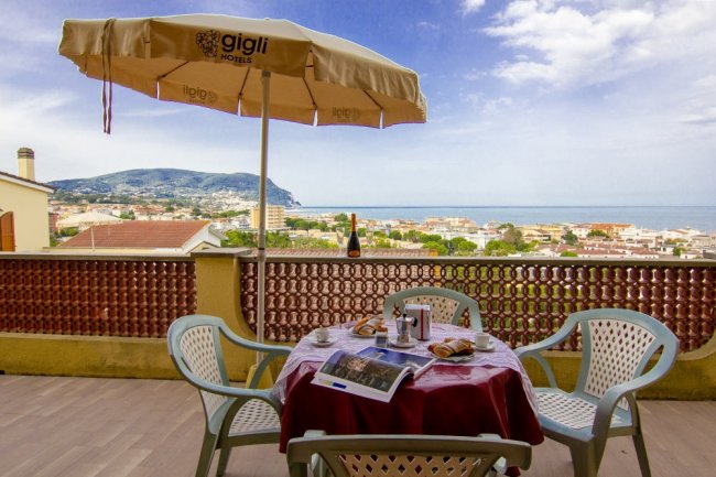 Vista mare dal balcone con tavolo e sedie sotto ombrellone.