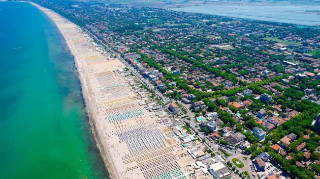 Vista aerea di una spiaggia affollata e città verdeggiante.