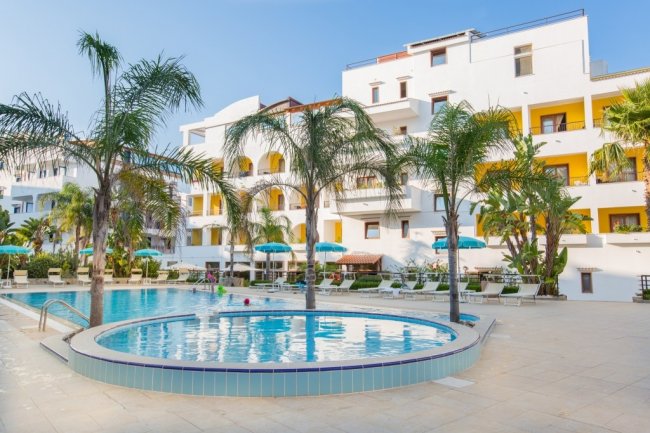 Piscina circondata da palme e hotel.