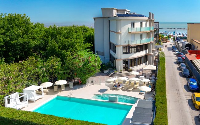 Vista aerea di piscina con edificio moderno e mare in lontananza.