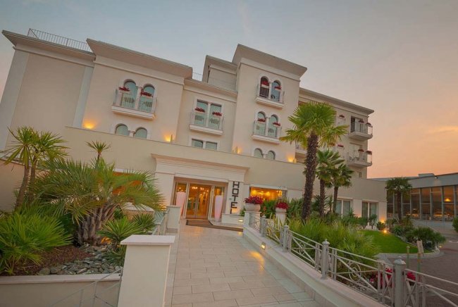 Ingresso di un hotel moderno con palme e luci accese.