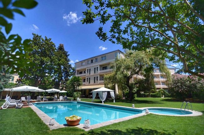 Piscina all'aperto con giardino e ombrelloni.