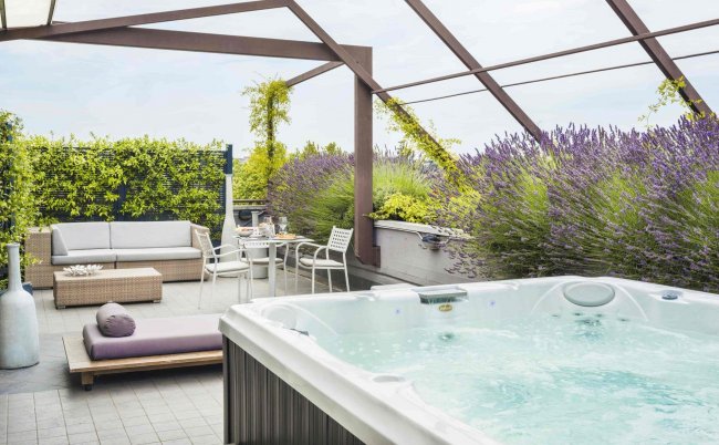 Terrazza con vasca idromassaggio, mobili da esterno e piante verdi.