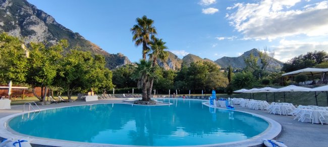 Piscina circondata da monti e alberi con cielo blu.