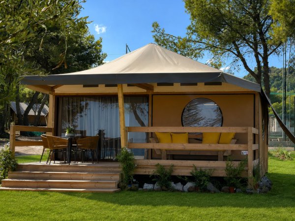 Una tenda in stile safari con veranda, circondata da alberi e prato verde.